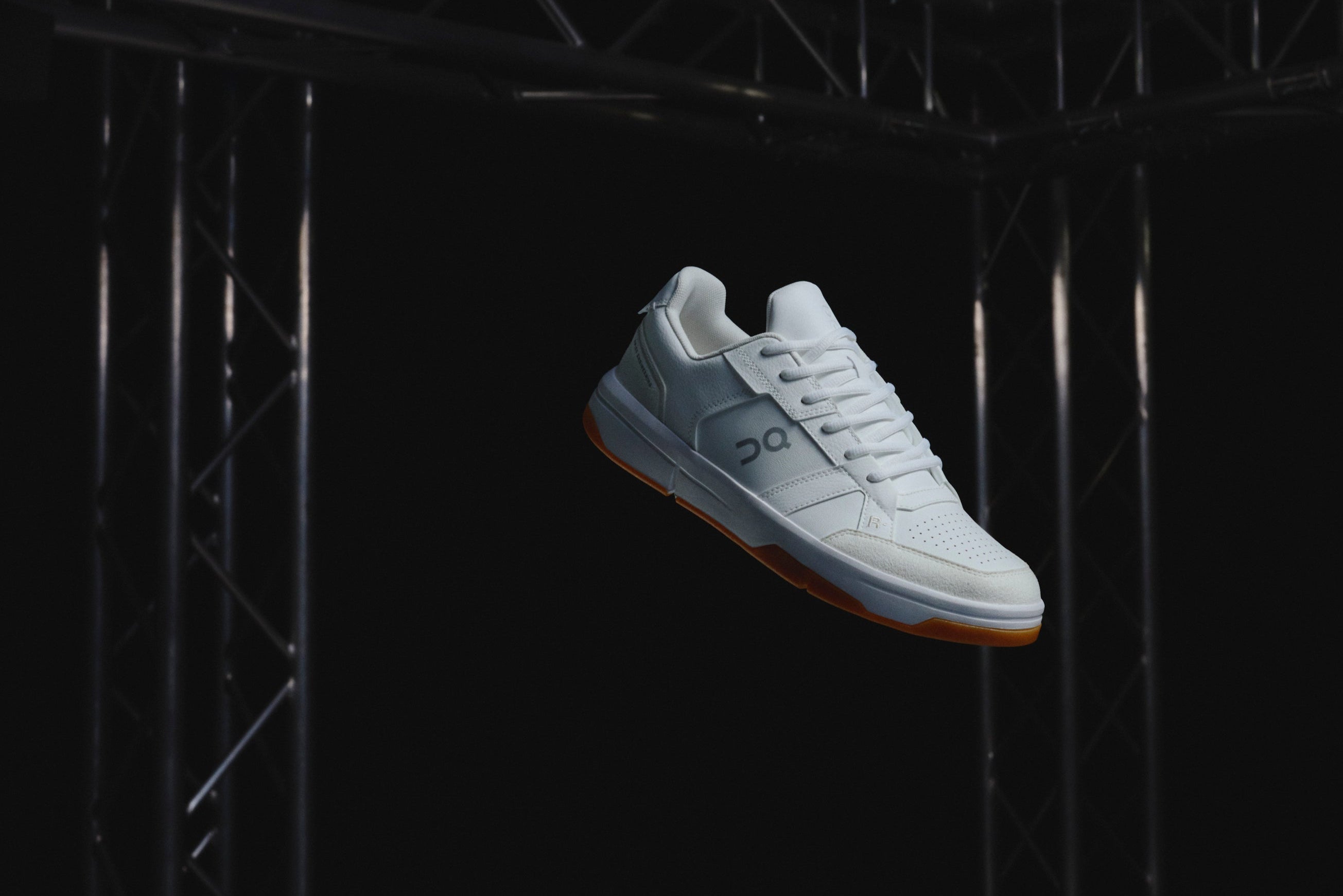 White sneaker hanging from a black metal structure against a dark background