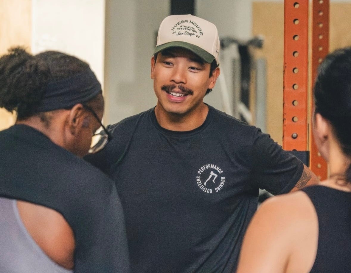 Man in a gym setting with two women, discussing athletic shoes.