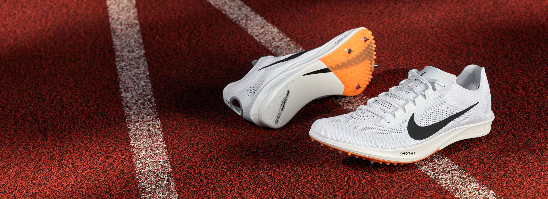 White running shoes with orange soles on a red track surface